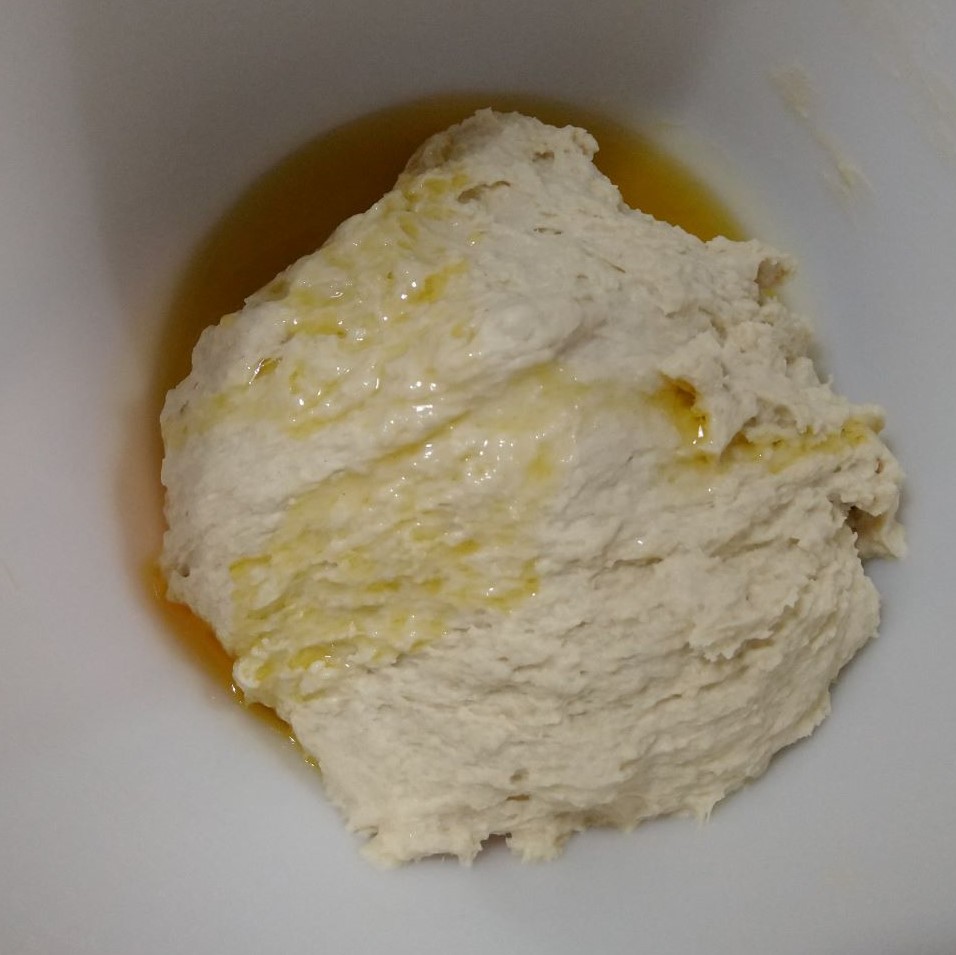 The olive oil is added to the dough in the mixing bowl.